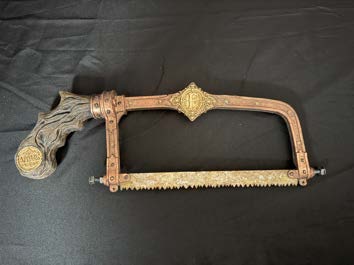 Close-up of the finished manual bone saw showing brass-toned fittings and a carved, weathered timber handle.
