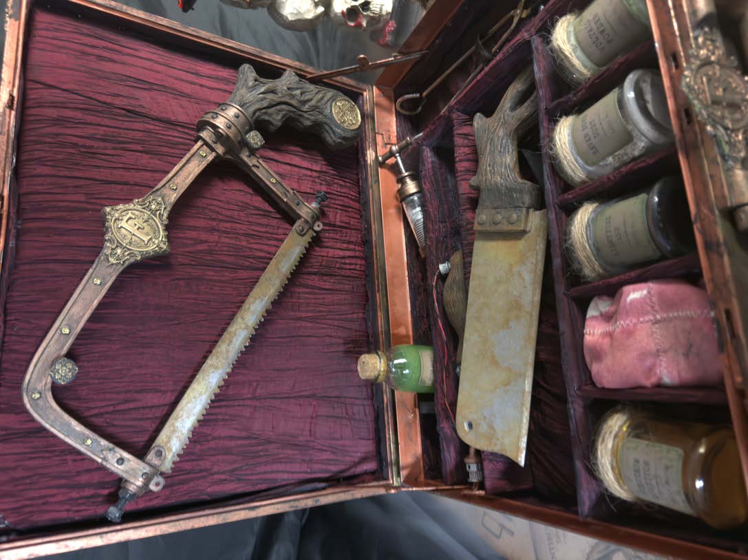 The completed prop kit laid out inside its custom-fitted case with burgundy lining, labelled containers and removable instruments.