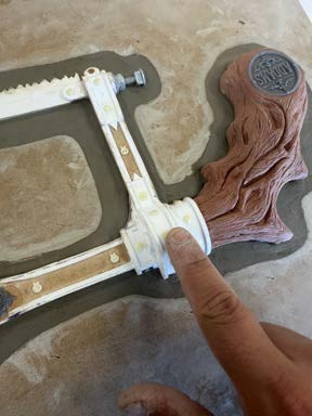 A hand applying rust and patina weathering effects to the assembled saw frame.