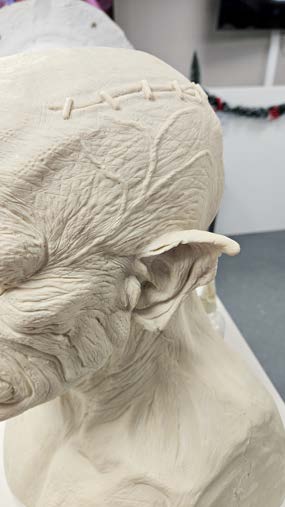 The character sculpted in grey clay, showing roughed-in ears, brow and jaw forms.