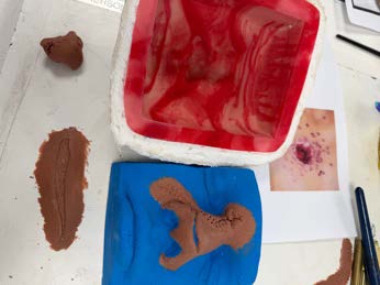 Prosthetic sculpts and moulds laid out on the bench alongside blood-effect materials.
