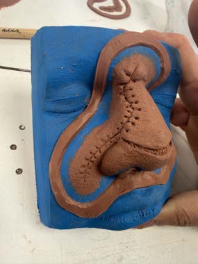 Prosthetic sculpt on a blue base with a clay flashing wall built around it.
